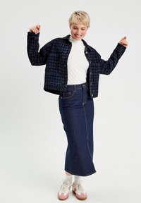 Veste en jean matelassée bleu foncé avec poches frontales, associée à une longue jupe en denim foncé. Un col roulé blanc et des baskets avec des accents roses complètent le look.
