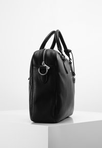 Schwarze Lederhandtasche mit genarbter Textur. Verfügt über abgerundete Griffe, silberne Beschläge und einen Reißverschluss oben. Der Boden ist flach.