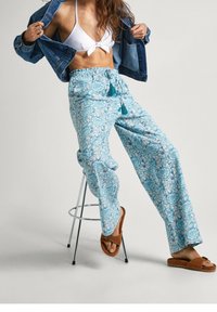 Světle modré vzorované kalhoty s květinovým designem, elastickým pasem a šňůrkou na stažení. Slučují se s bílým bikiny topem a džínovou bundou.