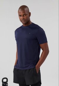 Tricou sportiv bleumarin, cu mâneci scurte, decolteu rotund și textură ușoară, asortat cu pantaloni șort negri. Include un logo subtil pe piept.