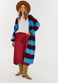 Długi sweter robiony na drutach w niebiesko-bordowe paski, połączony z białą bluzką i czerwoną satynową spódnicą, do tego beżowe botki do kolan.