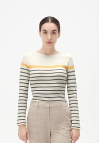 Pasiasty longsleeve w odcieniach kremowym, szarym i żółtym. Posiada okrągły dekolt i dopasowany krój, zestawiony z beżowymi spodniami w kratę.