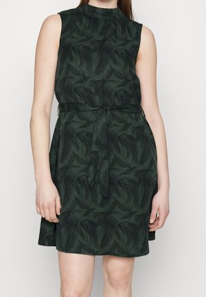 Vestido sin mangas de color verde oscuro con patrones negros de hojas y un cinturón a juego atado en la cintura, llevado por una persona que está de pie frente a un fondo liso.
