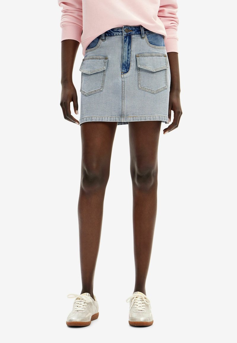 Gonna mini in denim azzurro chiaro con taglio dritto, due tasche frontali e chiusura con bottone anteriore. Abbinata a sneaker chiare.