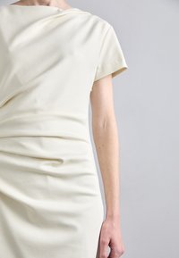 Krämbelagd klänning med korta ärmar, draperat tyg och midjeåtdragning. Slät yta, minimalistisk design, mångsidig för olika tillfällen.