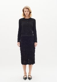 Cardigan nero a maniche lunghe con bottoni abbinato a una gonna a tubino floreale nera con texture. Ballerine nere a punta completano il look.