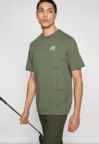 Μπλούζα από βαμβάκι σε ελιά πράσινο χρώμα με στρογγυλή λαιμόκοψη, κοντά μανίκια και λευκό κεντημένο λογότυπο στο αριστερό στήθος. Λεία υφή, casual εφαρμογή.