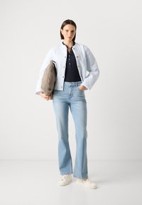 Chaqueta acolchada azul clara sobre un polo azul marino, combinada con jeans acampanados azul claros y zapatillas blancas. Sosteniendo un bolso gris con correas negras.