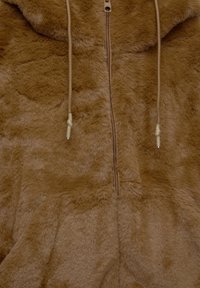 Veste marron pelucheuse avec fermeture éclair et deux cordons suspendus de chaque côté de la fermeture éclair.