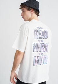 Biała bawełniana koszulka z krótkim rękawem, z wielokolorowym napisem na plecach: "MIND YOUR HEAD, WORK YOUR MIND", wyświetlanym pionowo.