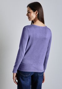 Lila långärmad tröja med rund halsringning och ribbad nederkant, tillsammans med mörkblå jeans, som visar en mjuk textur och avslappnad passform.