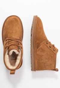 Paire de bottines en daim marron avec lacets sur l'avant et doublure en shearling moelleux, présentées vues de dessus et de côté sur fond blanc.
