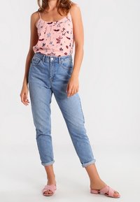 Camisola in satin rosa con motivo floreale, jeans in denim azzurro a vita alta e sandali a scivolo color blush con finitura testurizzata.
