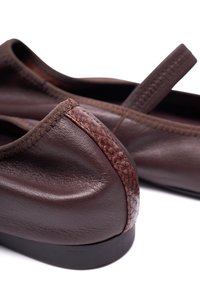 Zapatos de cuero marrón con una textura suave, acento trenzado en el talón y un diseño minimalista con una suela negra plana.