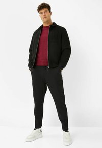 Schwarze Bomberjacke mit Reißverschluss, strukturiertes rotes Sweatshirt, schwarze Cargo-Hosen und weiße Sneaker. Minimalistisches Design, taillierte Silhouette.