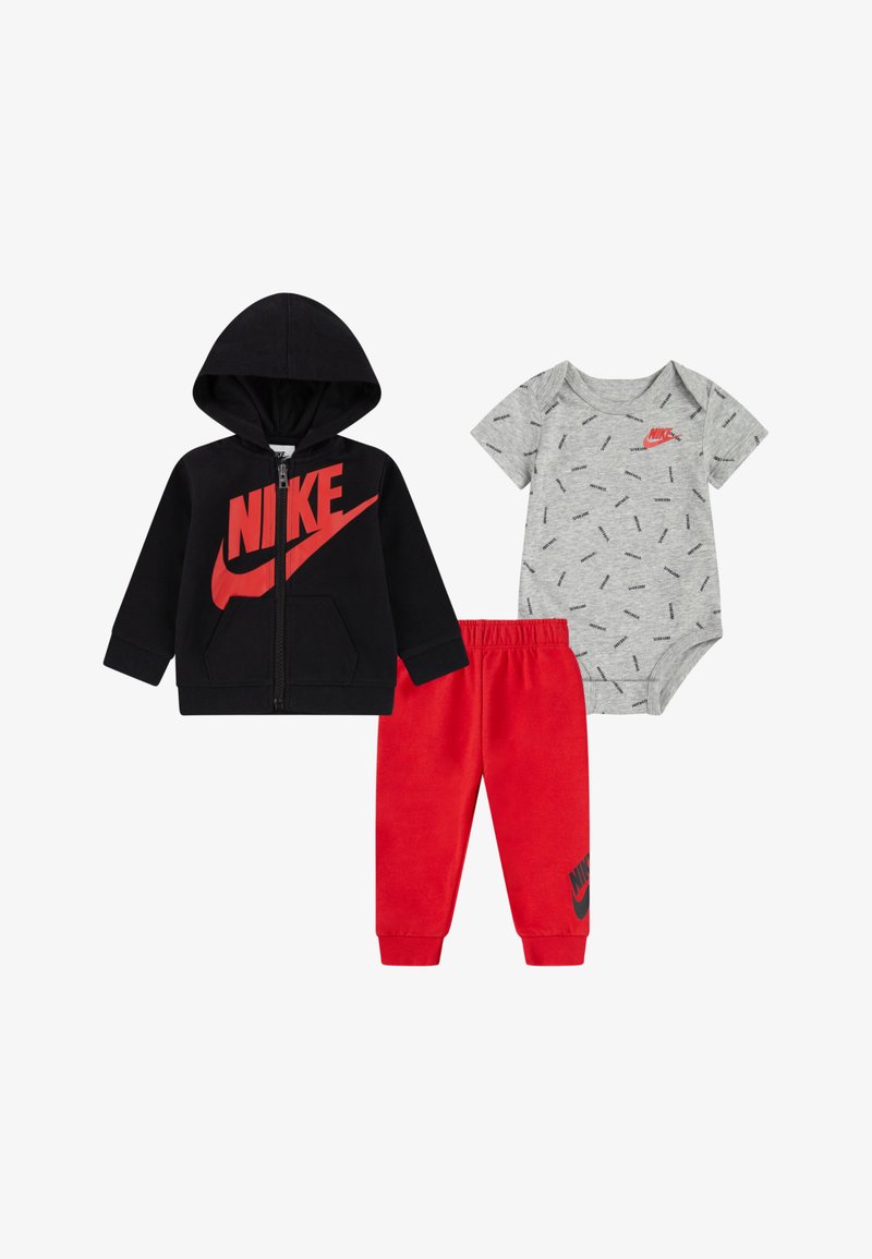 Nike otroška obleka: črna kapuca z zadrgo in rdečim logotipom, siva enodelna obleka s tiskanim vzorcem in rdeče trenirke z logotipom na gležnju.