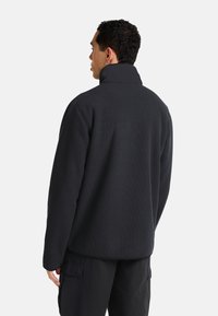 Pullover nero a coste con colletto alto, caratterizzato da una vestibilità comoda e una superficie testurizzata, abbinato a pantaloni cargo.