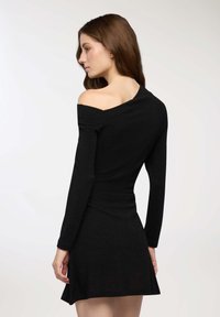Czarna dzianinowa sukienka z długimi rękawami, projekt z dekoltem off-the-shoulder, dopasowana w talii i rozkloszowana u dołu, z delikatnym połyskiem w tkaninie.
