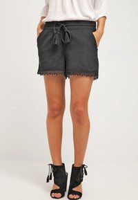 Czarne plecione szorty ze ściągaczem w talii i koronkowym wykończeniem. Połączone z czarnymi otwartymi botkami na obcasie z ozdobnymi frędzlami.