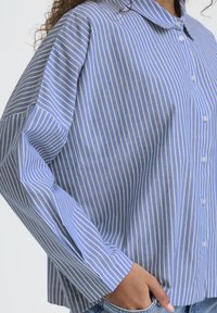 Blå skjorte med knapper i stribet mønster, rundet krave og lange ærmer, med tynde hvide striber og en afslappet pasform.