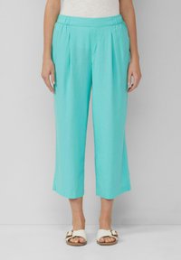 Pantaloni cropped turchesi con fronte plissé, elastico in vita e tessuto leggero. Abbinati a sandali bianchi con una fibbia marrone.