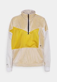 Lättviktig jacka med halvmidja och en färgsättning i kräm och klart gult, nätpaneler, elastiska manschetter och en liten logotyp på den nedre sidan.