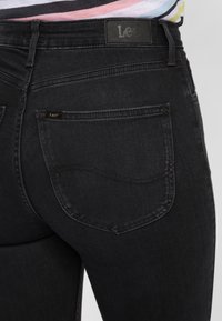 Jeans in denim nero presentano una texture liscia, un design standard a cinque tasche e una vita con marchio caratterizzata da un logo discreto.