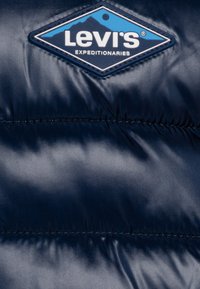 Navyblå vadderad tyg med en diamantformad Levi's Expeditionaries-logotyp med bergdesign.