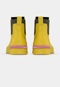 Bottes de cheville en caoutchouc jaune avec un détail rose sur la semelle, présentant une texture lisse et des languettes à l'arrière pour faciliter l'enfilage et le retrait.