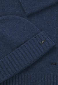 Navy knit beanie and sweater set, featuring a ribbed cuff and a small metallic brand label, made from soft, textured fabric.