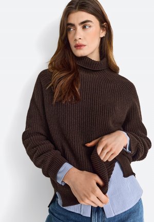 Maglione a coste marrone con colletto alto, indossato sopra una camicia a righe blu e bianca. Il design presenta maniche ampie e una vestibilità rilassata.