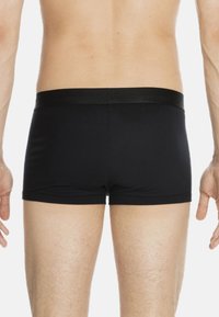 Mann in schwarzen enganliegenden Boxershorts, von hinten gezeigt, vor einem schlichten weißen Hintergrund.