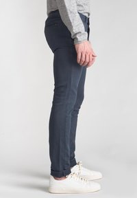 Jeans slim fit blu scuro con una texture liscia, caratterizzati da tasche posteriori e orli arrotolati, abbinati a sneakers bianche basse.