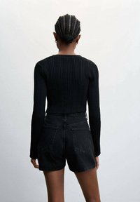 Černý žebrovaný top s dlouhým rukávem v kombinaci s vysokým pasem černými džínovými šortkami, které vykazují obtaný siluetu a texturovanou tkaninu.