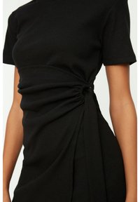 Robe noire à rayures avec des manches courtes ; présente des détails froncés à la taille avec un accent torsadé, créant une texture drapée.