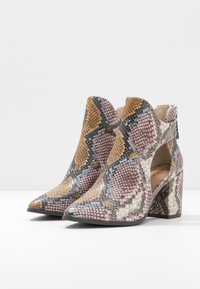 Botines de piel de serpiente con punta afilada, con una textura estampada en rosa, marrón y gris, y un tacón grueso para soporte.