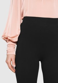 Zwarte fitted broeken gecombineerd met een roze satin blouse met pofmouwen en geplooide manchetten, die gladde texturen en contrasterende kleuren benadrukt.