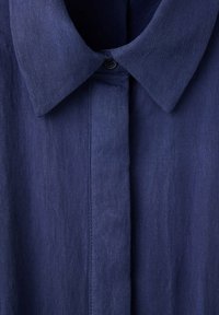 Col de chemise bleu foncé avec fermeture par bouton et patte de boutonnage dissimulée en tissu léger.