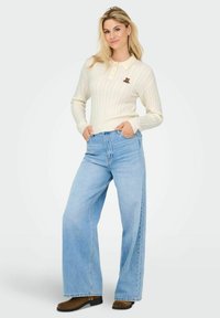 Kremeni džemper s pletenim uzorkom i ovratnikom, uparen s ljubičasto-plavim širokim trapericama i smešnim gležnjačama.