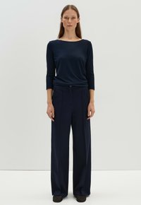 Diepblauwe langemouwen top met een brede halslijn, gecombineerd met hoge taille, wijde broek in een bijpassende kleur. Glad, zacht stoftextuur.