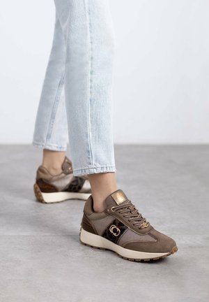 Brown sneaker with mesh and suede materials, gold accents, and leopard print detail. White sole with textured grip. Styled with light denim.