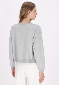 Grauer, kurz geschnittener Sweatshirt mit langen Ärmeln, gerippten Bündchen und Saum. Glatte Textur, minimalistisches Design. Kombiniert mit weißen Hosen.