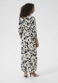 Maxi dress in cream with black and light blue floral print, featuring a cinched waist, long sleeves, and a relaxed fit.