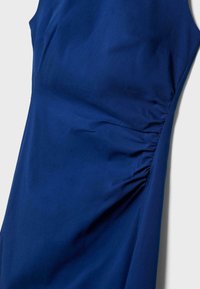 Robe bleue sans manches avec détail de tissu froncé sur le côté droit, texture lisse et silhouette ajustée sur un fond clair.