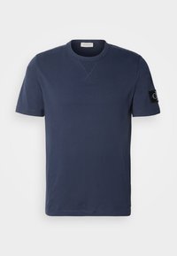 T-paita lyhyillä hihoilla, tummansininen, pyöreä pääntie, ribbausta kauluksen alla ja musta Calvin Kleinin logopainatus vasemmassa hihassa.