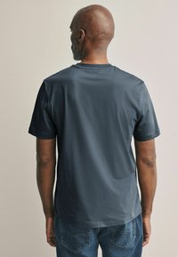 Camiseta de algodón en azul oscuro, de manga corta, con cuello redondo, textura suave, combinada con jeans de mezclilla que cuentan con bolsillos traseros cosidos.