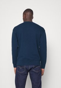 Sweatshirt bleu marine avec un col rond, des poignets et un ourlet côtelés, fabriqué en tissu doux. Associé à un jean en denim bleu foncé montrant des poches arrière.