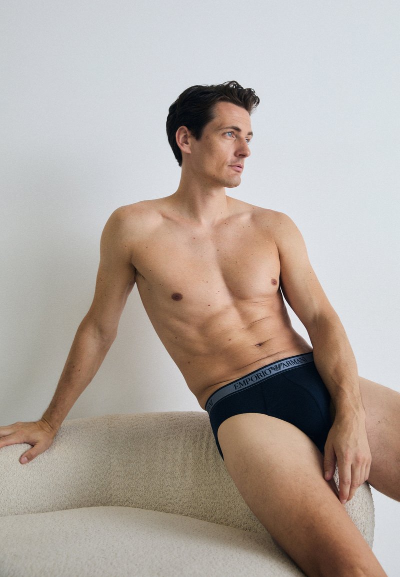 Sötétkék Emporio Armani alsónadrág logózott elasztikus derékpánttal. Az anyag simának és testhezállónak tűnik, hangsúlyozva a modell alkatát.