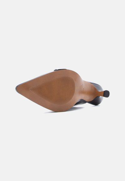 Μαύρο ψηλοτάκουνο παπούτσι που είναι ξαπλωμένο στο πλάι, δείχνοντας μια λεία καφέ σόλα με λεπτές οριζόντιες αυλακώσεις στην περιοχή του μπροστινού μέρους του ποδιού.