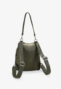 Bolsa de nailon verde oliva con correas ajustables, textura suave, detalles en hardware plateado y un bolsillo con cremallera lateral.